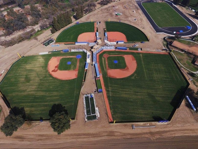Aerial view of four baseball/softball fields with green outfields and brown infields in a complex