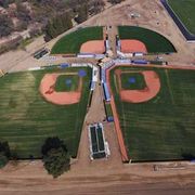 Aerial view of two adjacent baseball fields with green outfields, red infields, and a central walkway