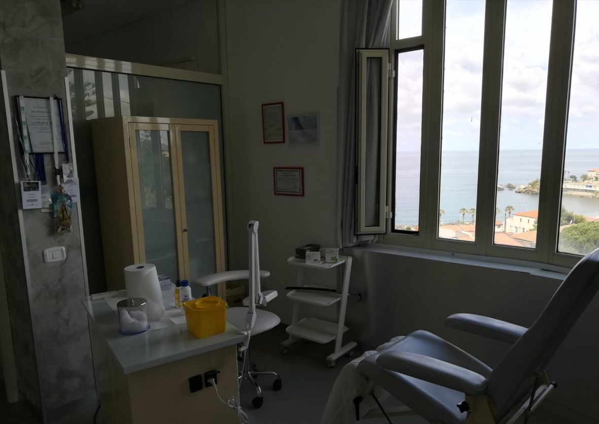 Sala per visite odontoiatriche con poltrona, lavandino, carrello e ampie finestre con vista sull'acqua.