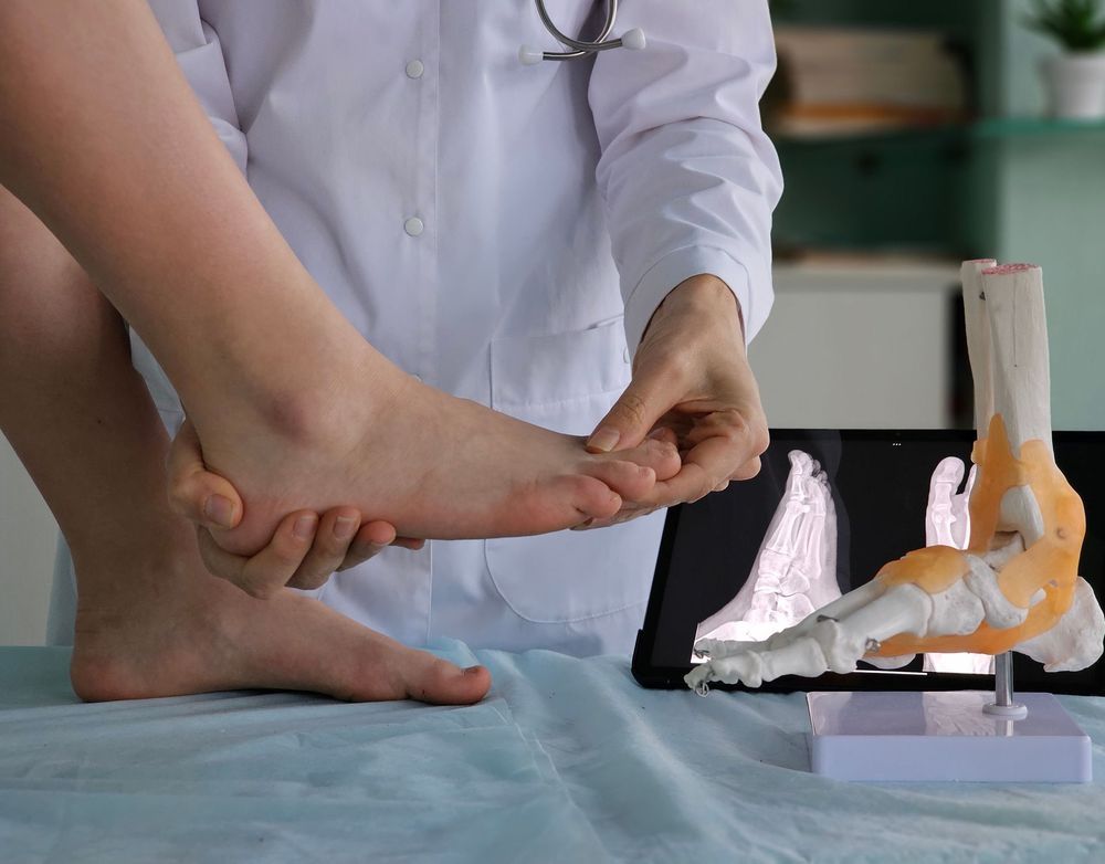 Un medico esamina la caviglia di un paziente accanto a un tablet che mostra un modello anatomico del piede.
