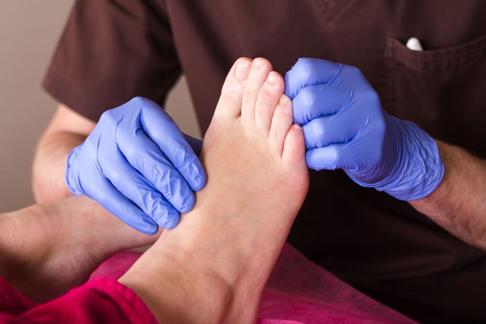 Mani guantate che massaggiano un piede nudo durante un trattamento di pedicure.