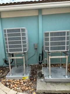Two air conditioning units on metal platforms against a turquoise wall.