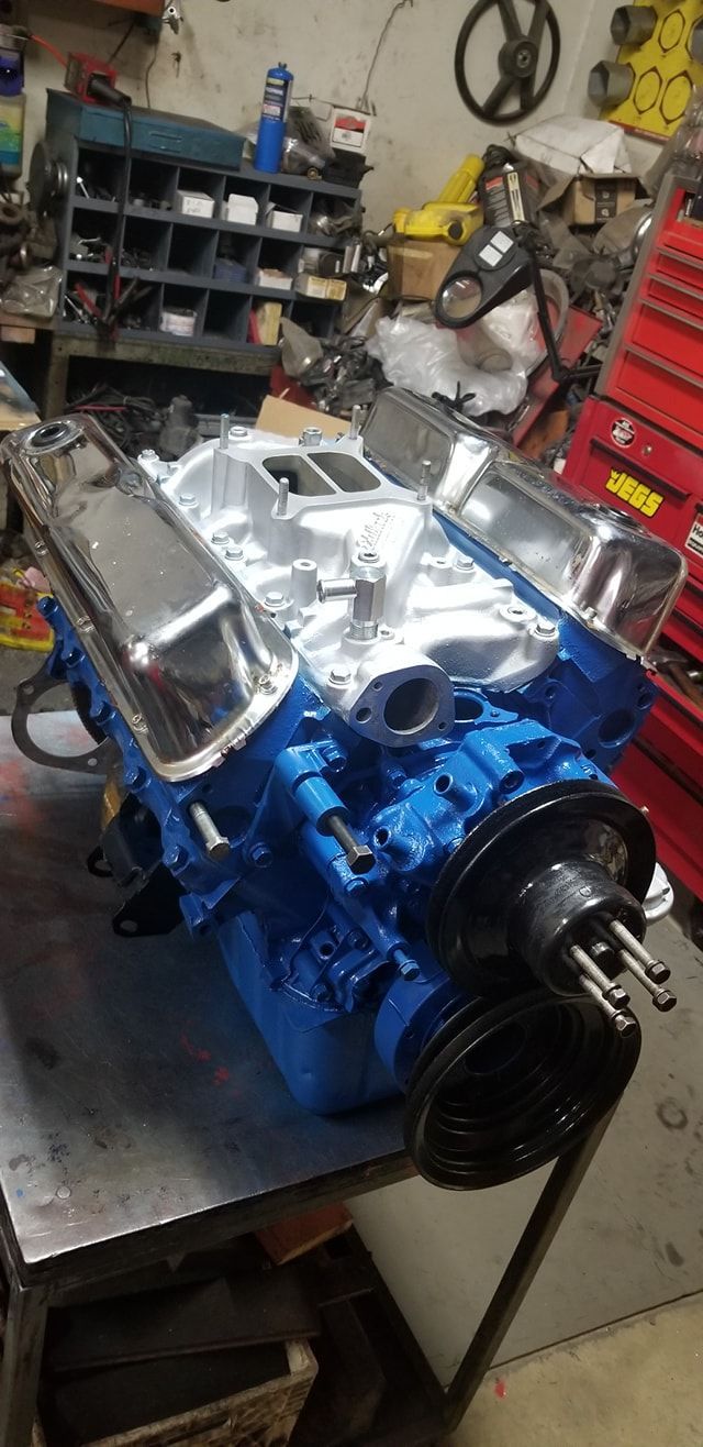 A freshly rebuilt blue V8 engine block with chrome valve covers, sitting on a metal workbench in a garage.