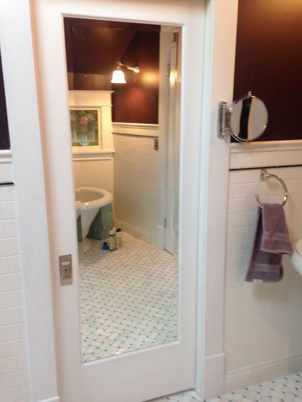 White bathroom with partially visible mirror door; white and patterned floor; purple towels.