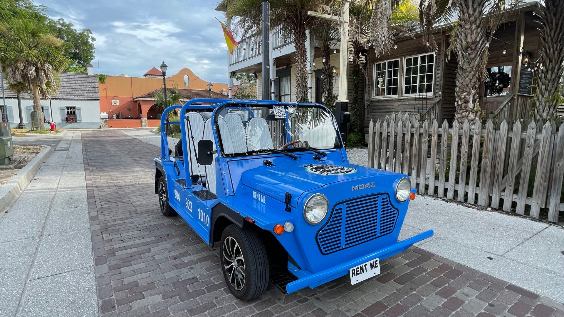 A blue electric moke is parked on a cobblestone road in front of a building in saint augustine florida