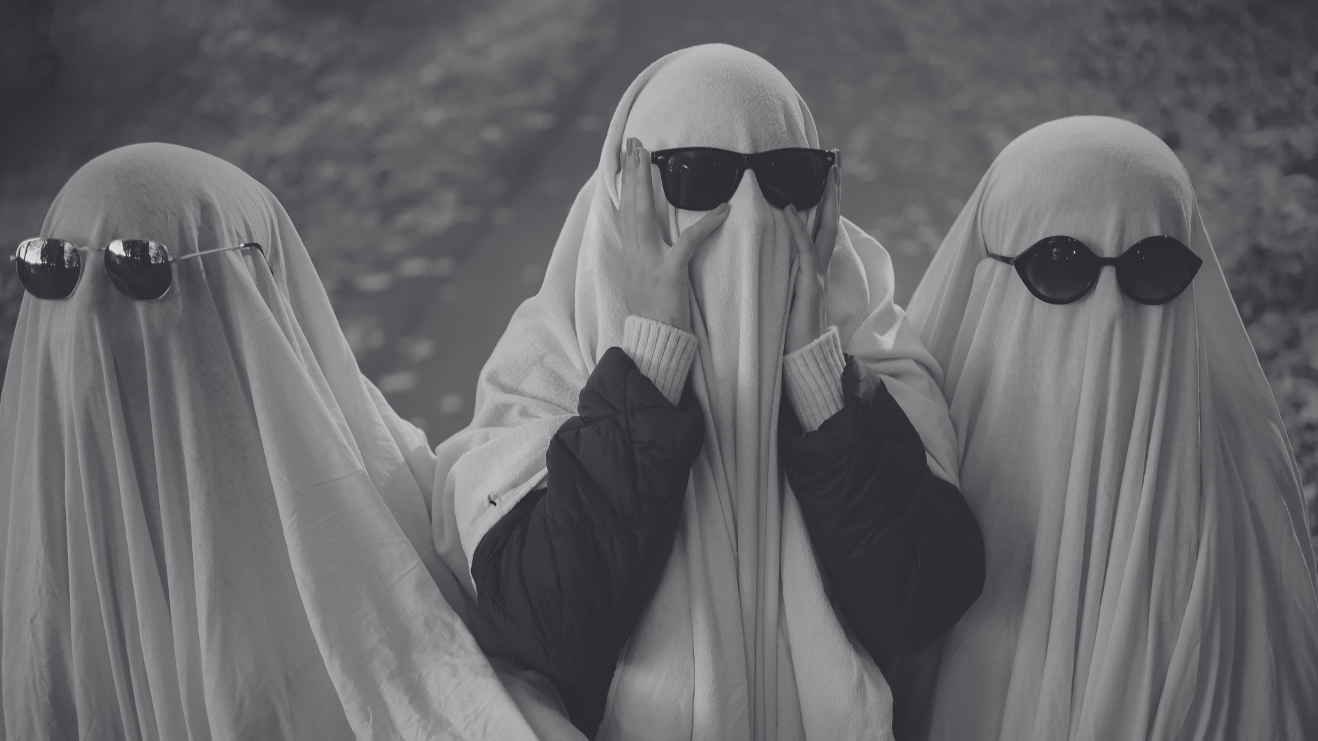 Three veiled figures in sunglasses stand side by side in grayscale.