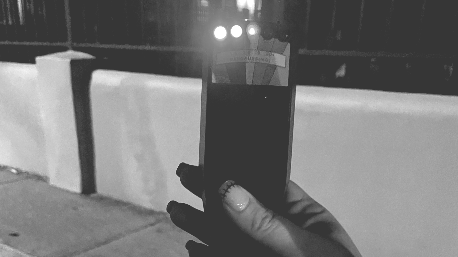 Hand holding a phone in front of a lit barrier at night