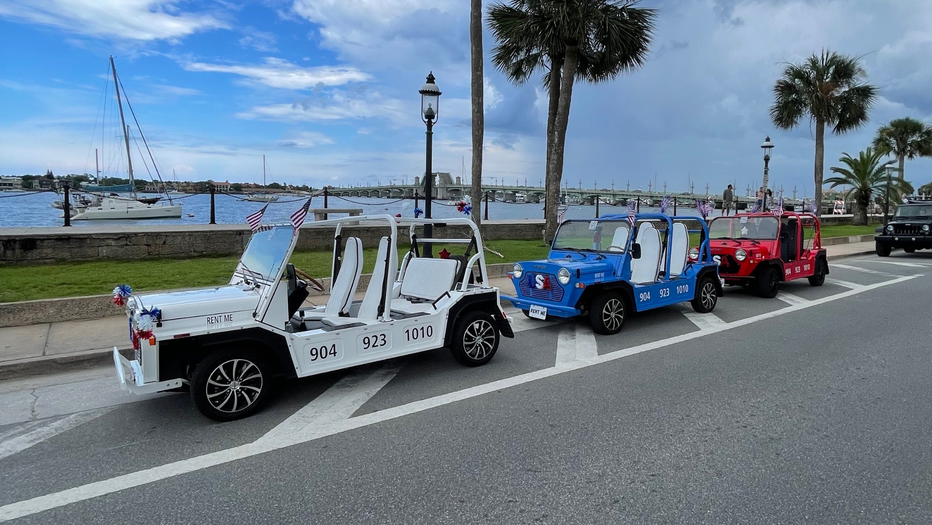Three electric moke's are parked on the side of the road near the bay in saint augustine florida