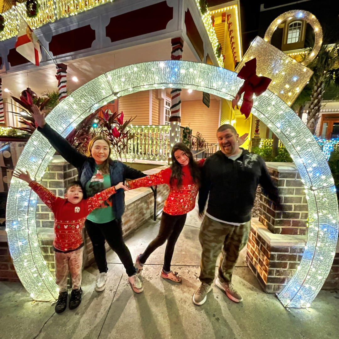 Family posing inside a lit Christmas ornament arch. Festive lights and decorations. St. Augustine