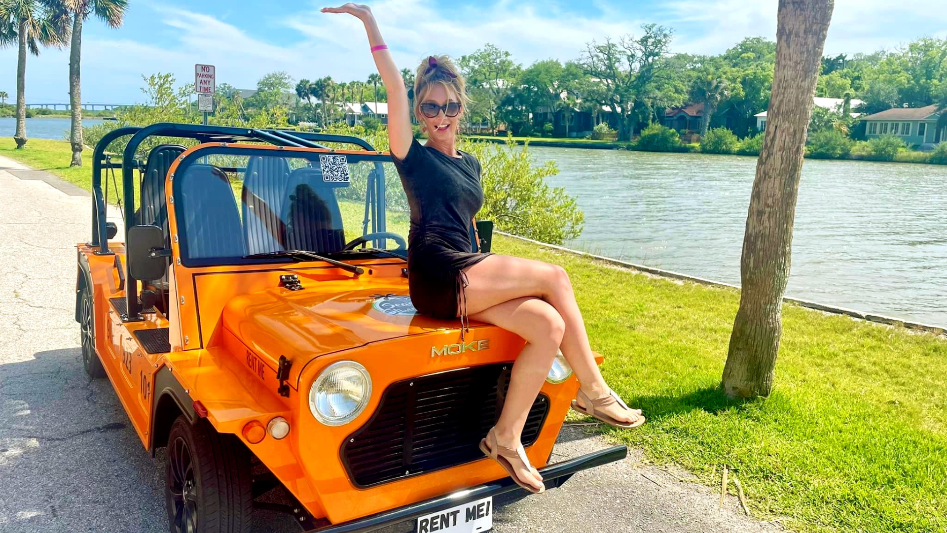 A woman is sitting on the hood of an orange electric moke in saint augustine florida