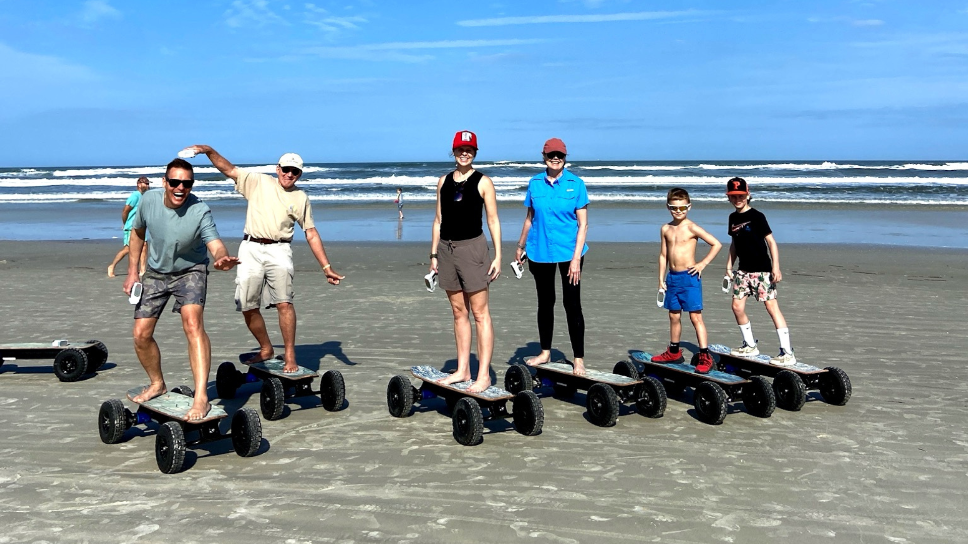 People standing on off-road electric scooters on a sandy beach near the waterline