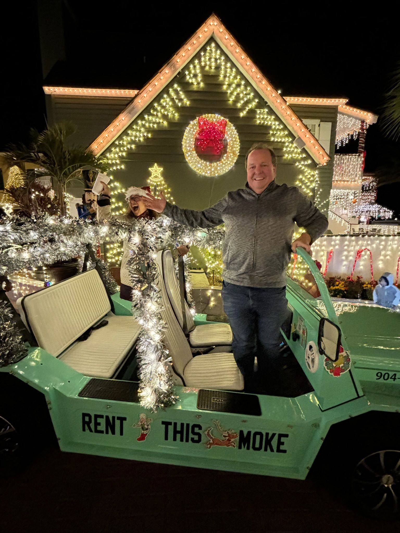 Man standing in a teal golf cart decorated with lights, in front of a house lit with Christmas lights in St. Augustine. 
