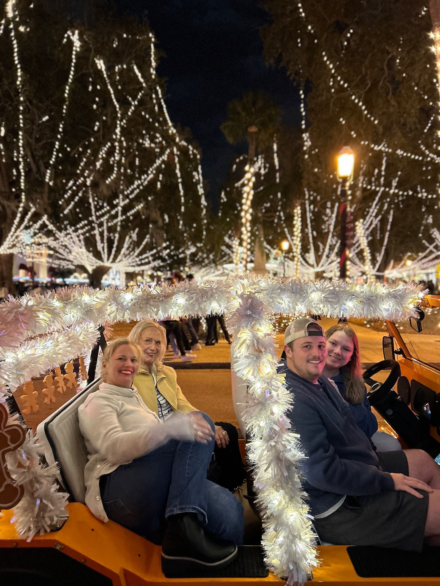 People ride in a festive lit Moke at night. Trees are adorned with white lights. Nights of Lights St. Augustine Tour.