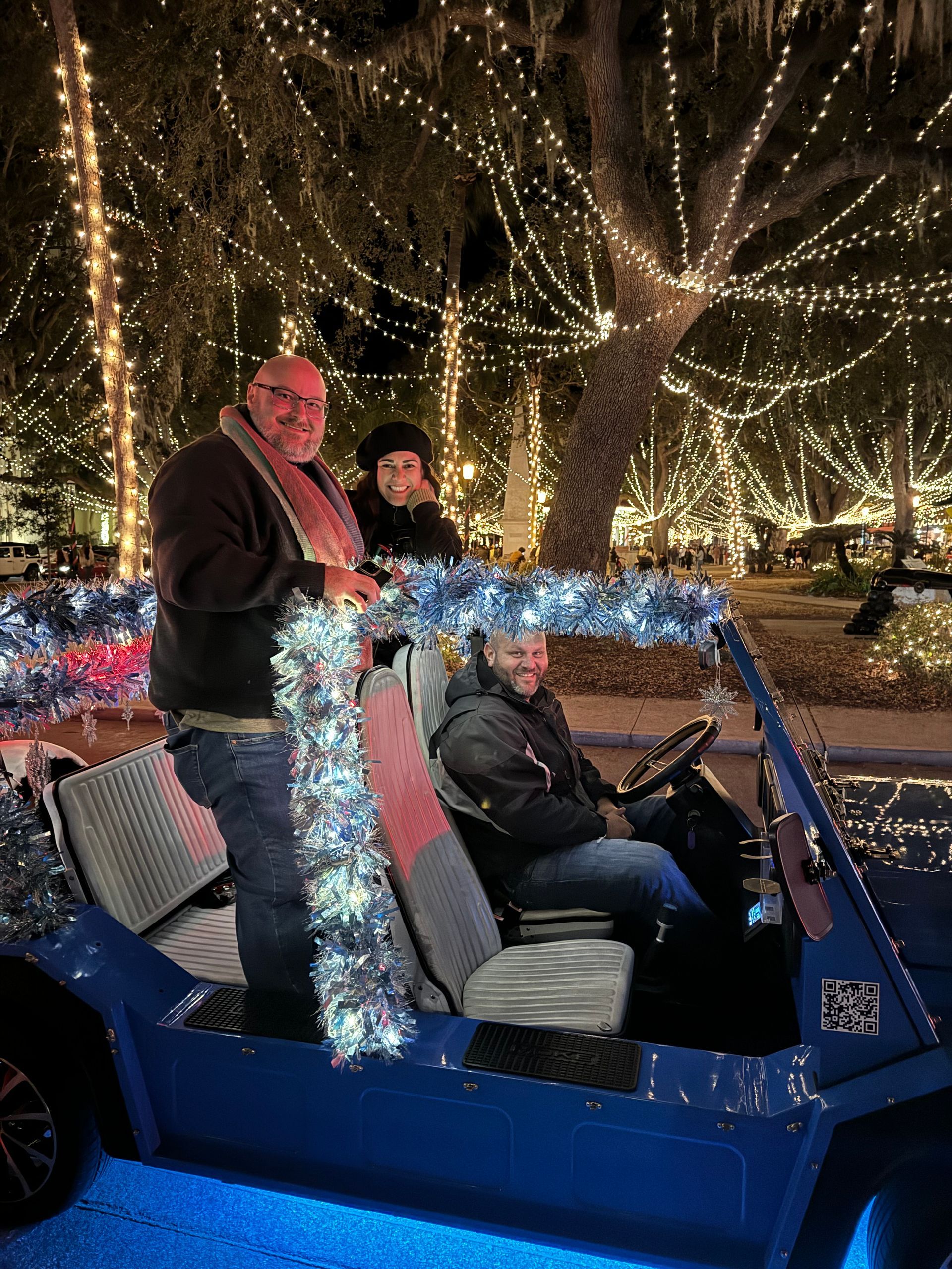 Three people in a blue golf cart decorated with lights, driving at night at St Augustine's Nights of Lights