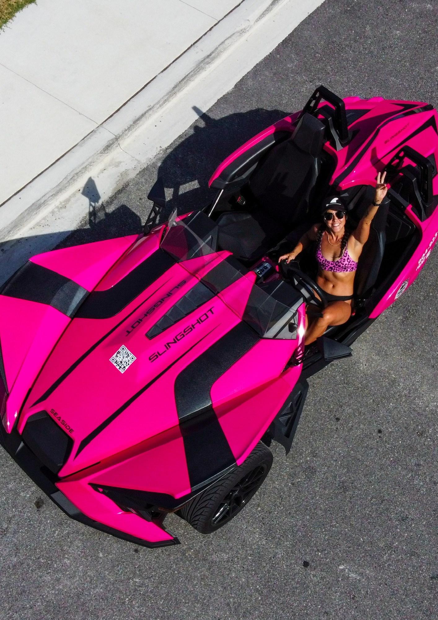 Bright pink and black sports car parked by a curb with its door open and a person inside