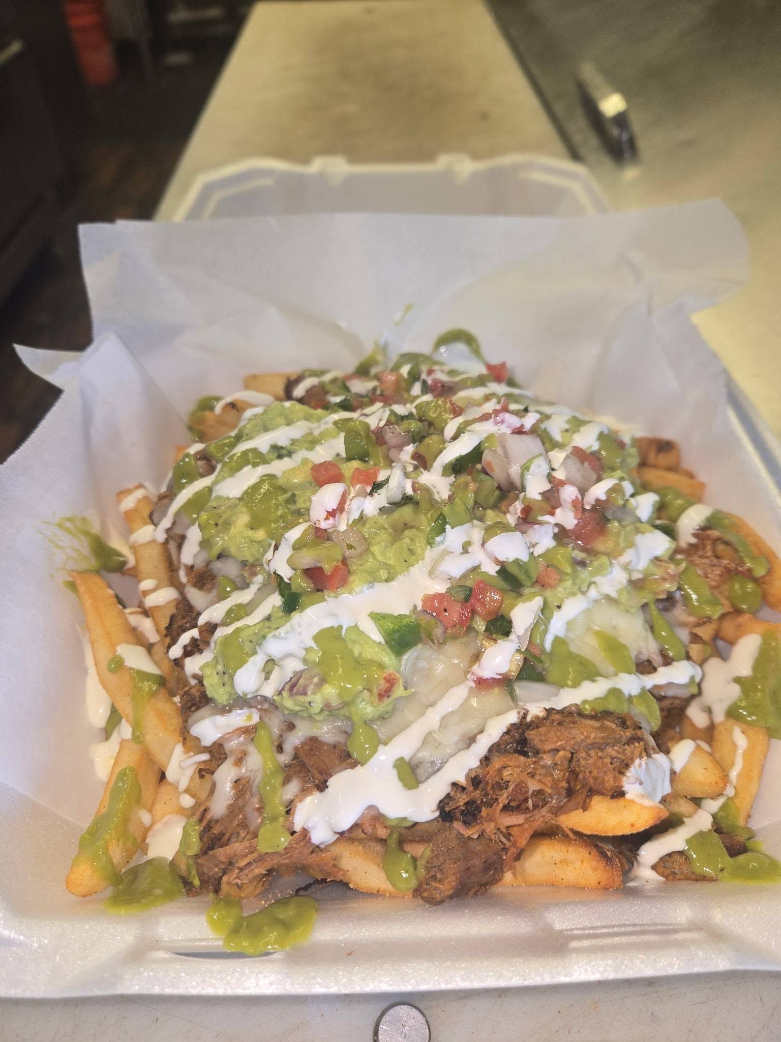 Loaded fries topped with green sauce, white drizzle, and diced onions in a takeout tray