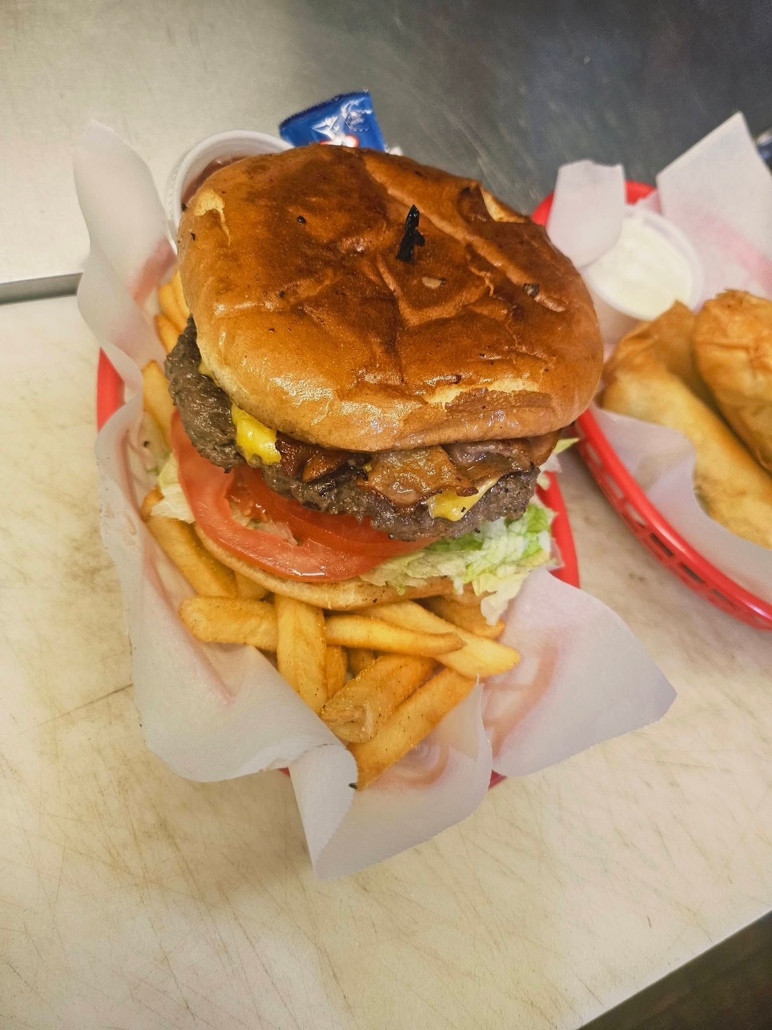Burger with fries in a paper wrapper on a table, with ketchup packets nearby