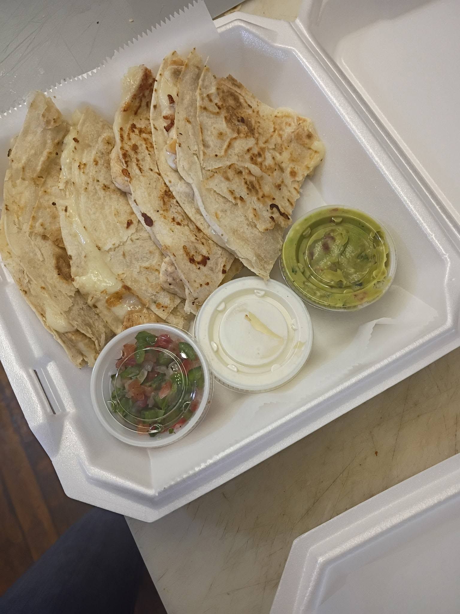 Folded flatbread on a takeout tray with three small sauce cups: green chutney, white sauce, and salsa.