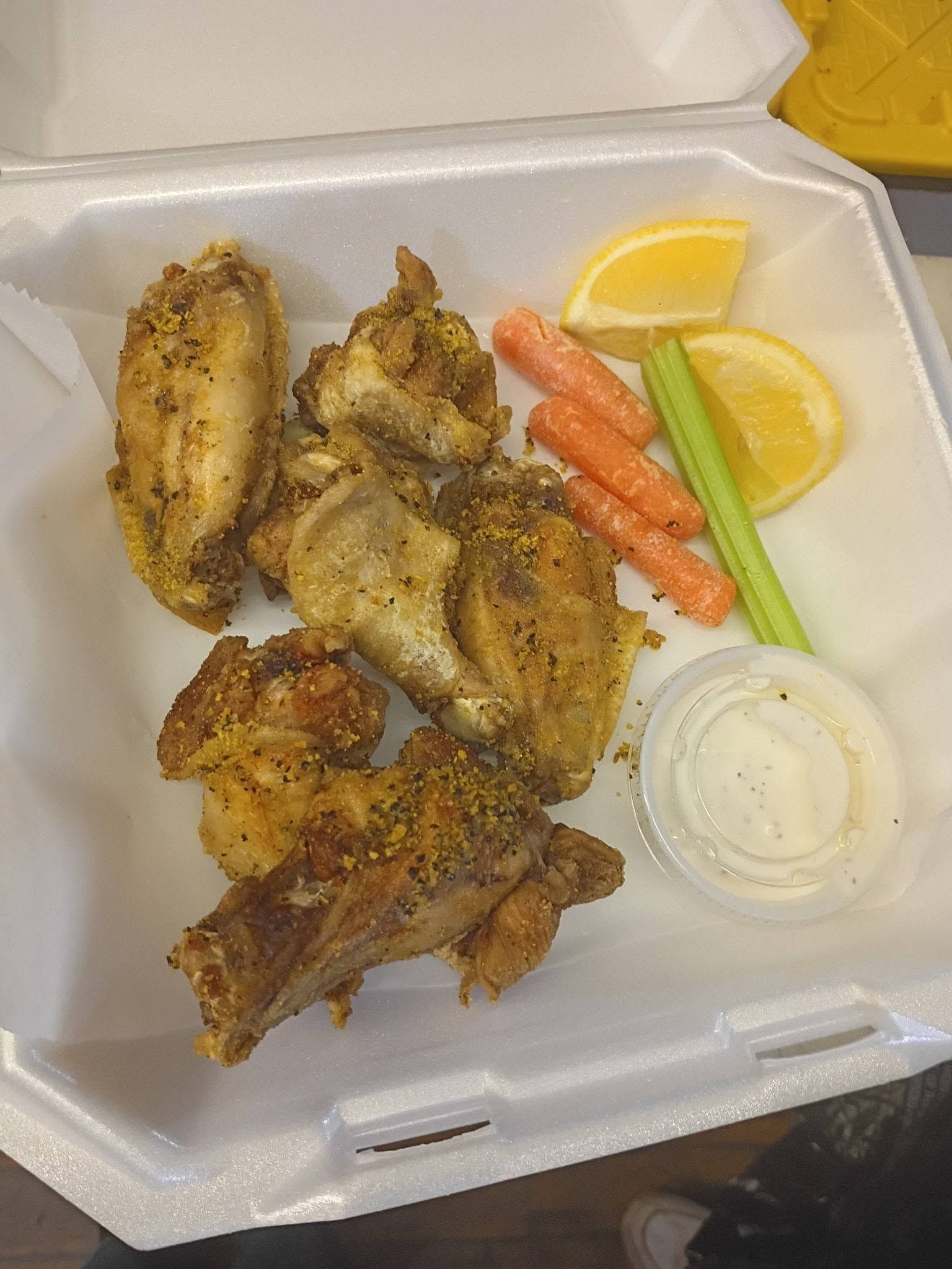 Takeout box with seasoned chicken wings, carrot sticks, celery, lemon wedges, and dipping sauce