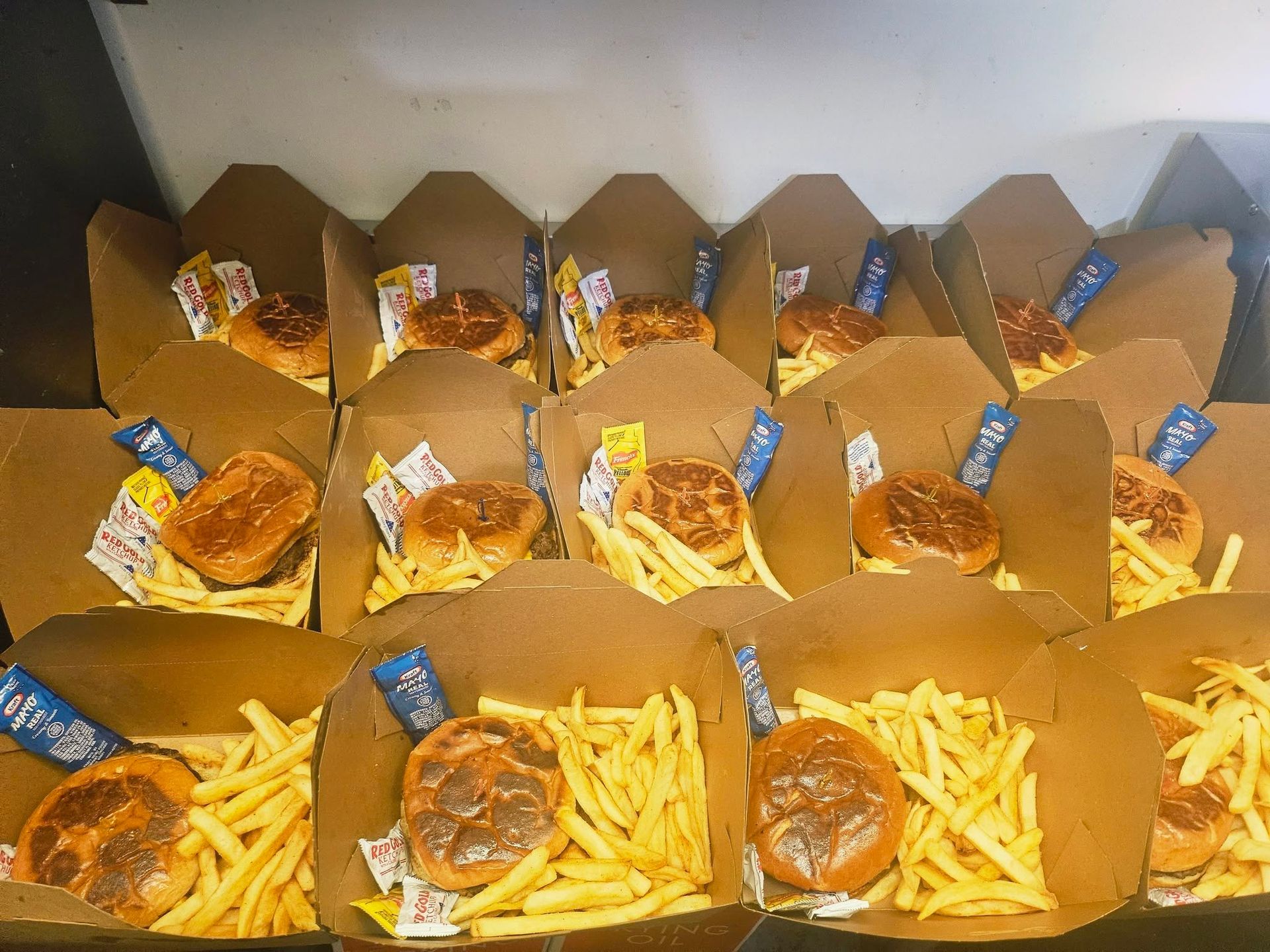 Rows of open takeout boxes filled with burgers and fries on a table