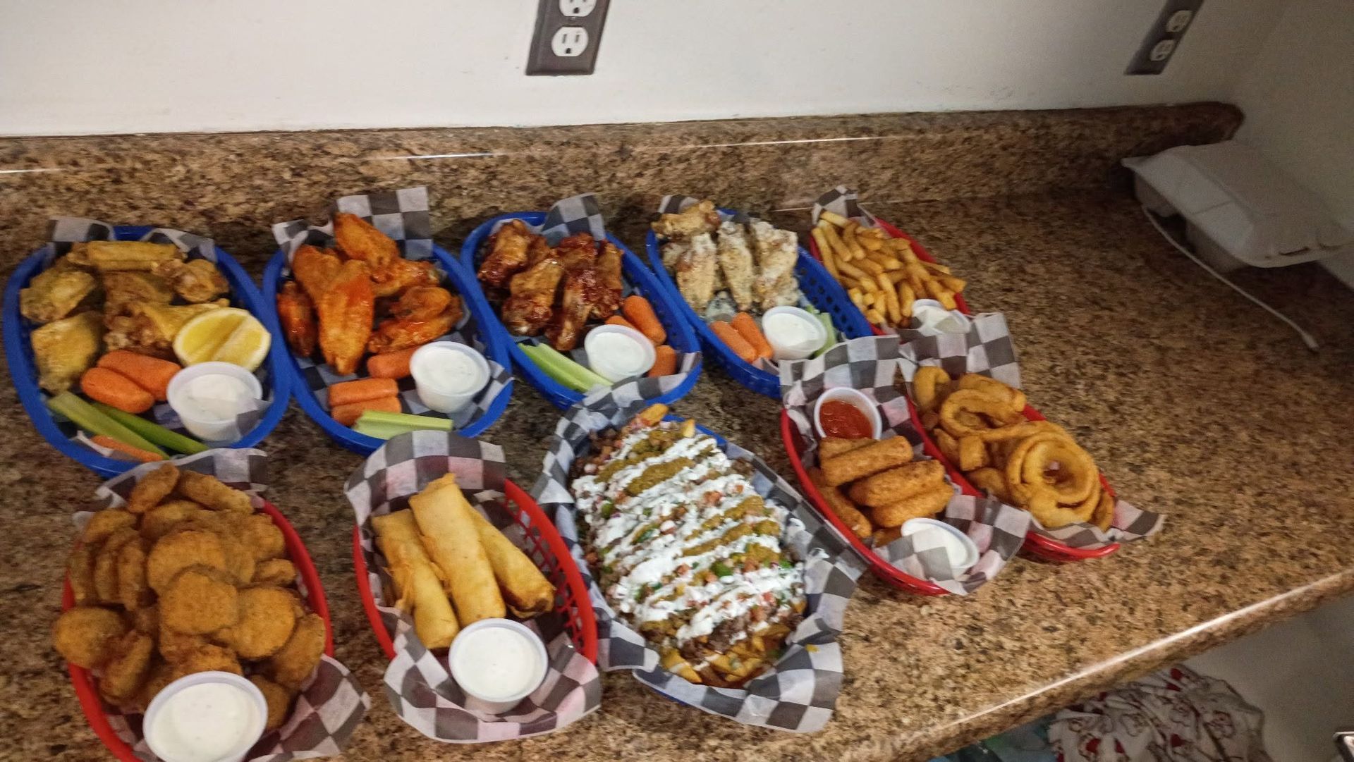 Trays of assorted fried foods and breads arranged on a kitchen countertop with dipping sauces