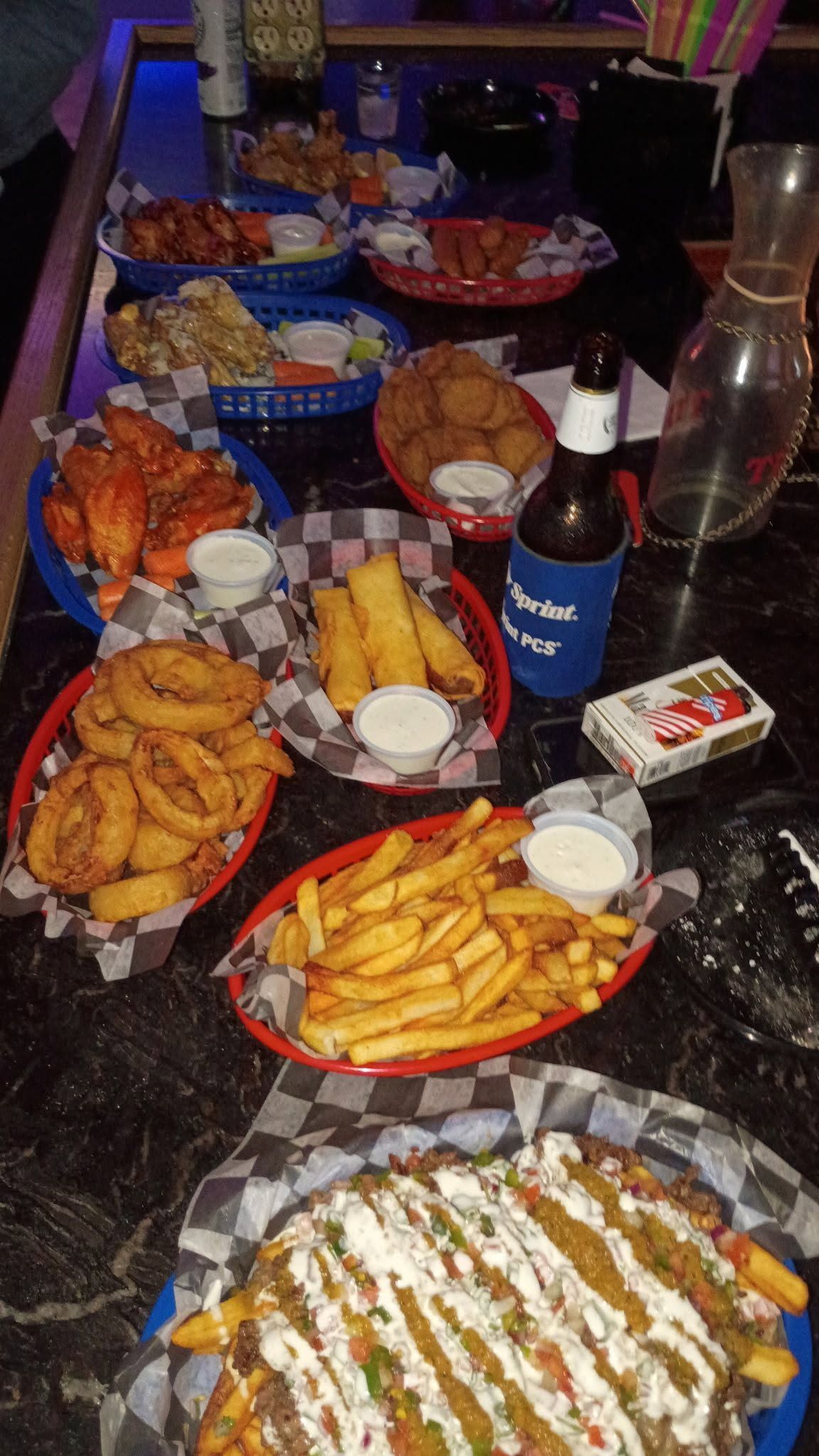 Table covered with assorted snacks and drinks on plates and trays, including fries, pastries, and a bottle of wine.