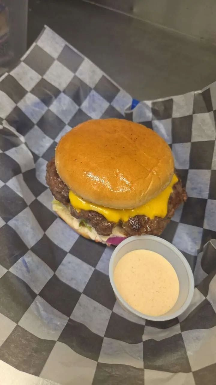 Cheeseburger with glossy bun and dipping sauce on black-and-white checkered paper tray