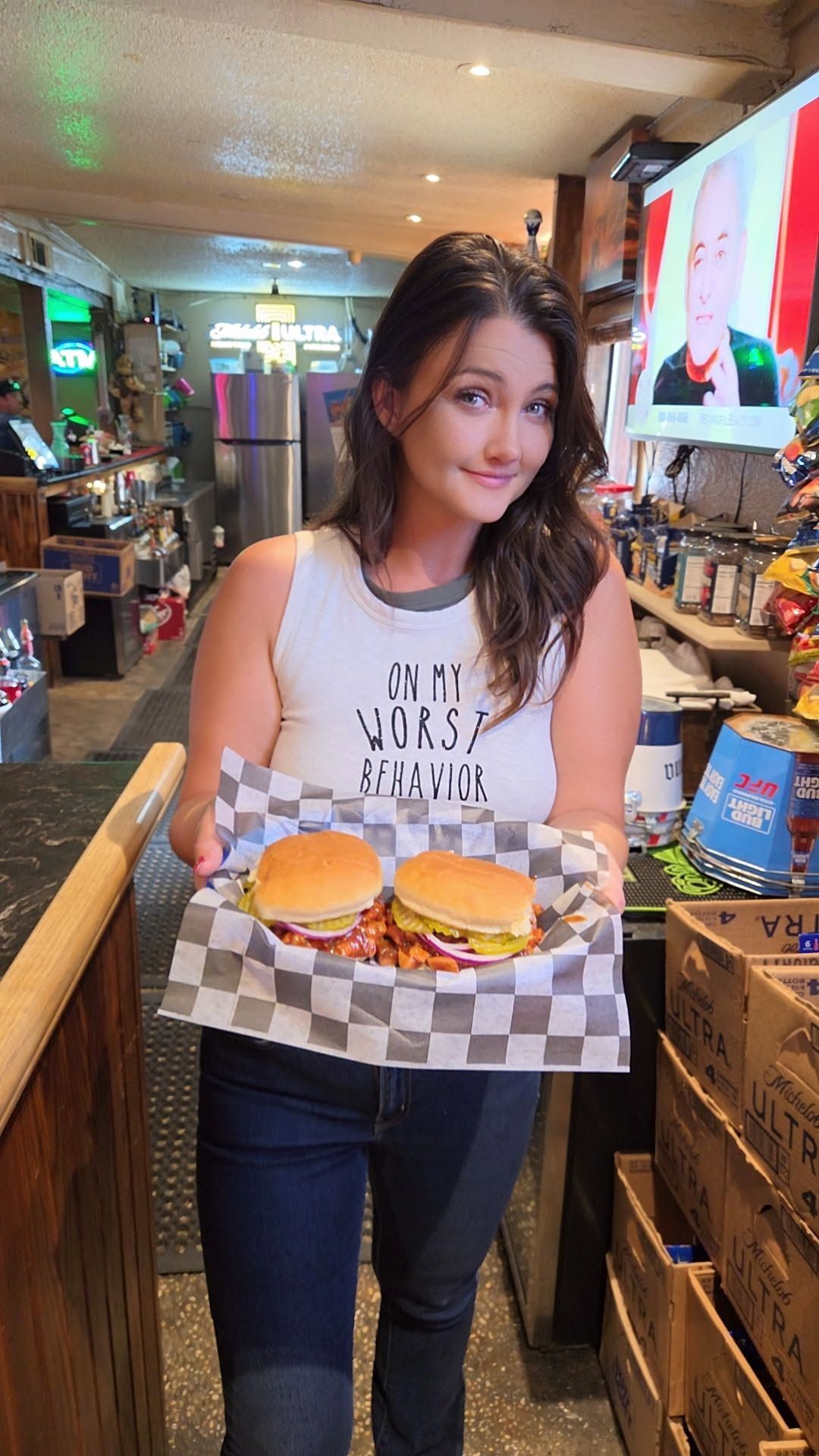 Smiling woman in a cafe holding a tray with two burgers and checkered paper wrapping