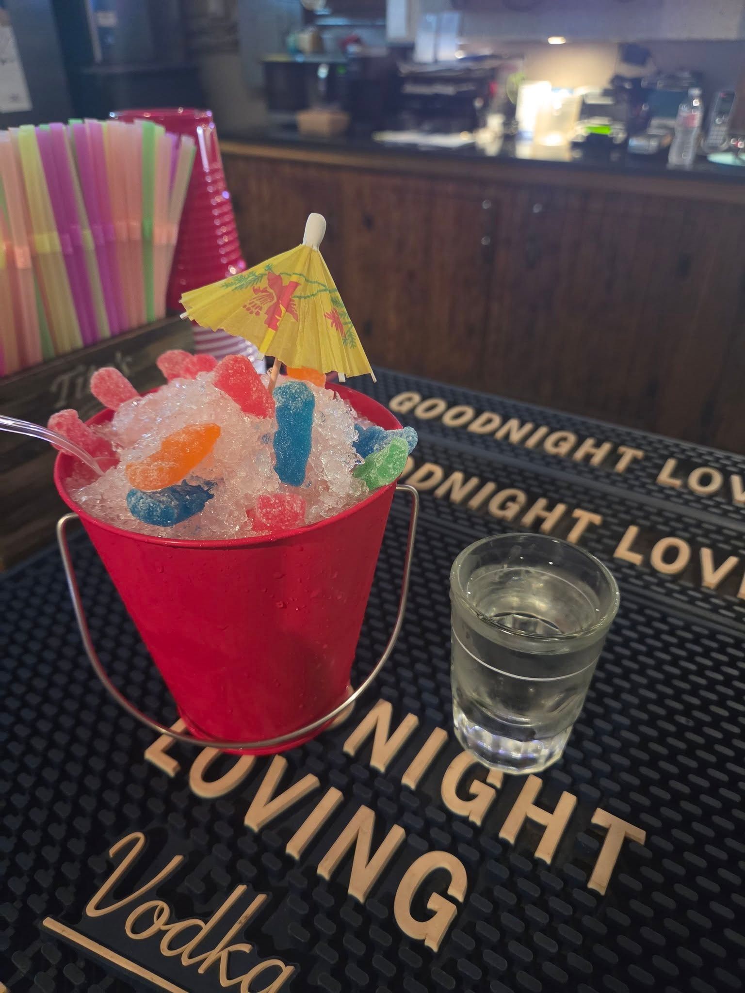 Red cup of colorful gummy candy on a bar tray with a shot glass and “Goodnight Loving Vodka” text