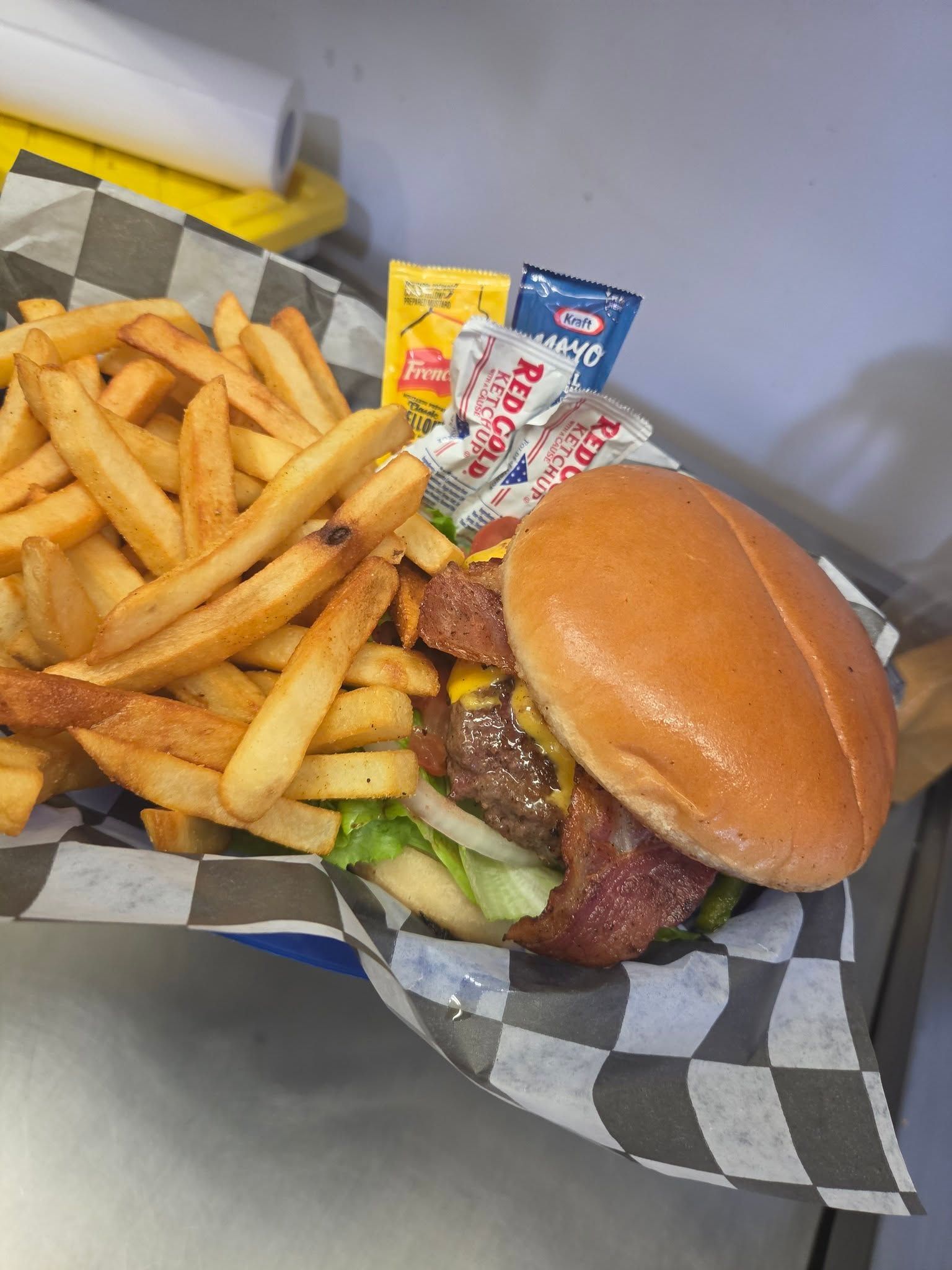 Burger and fries in a checkered tray, with ketchup and condiment packets on the side.