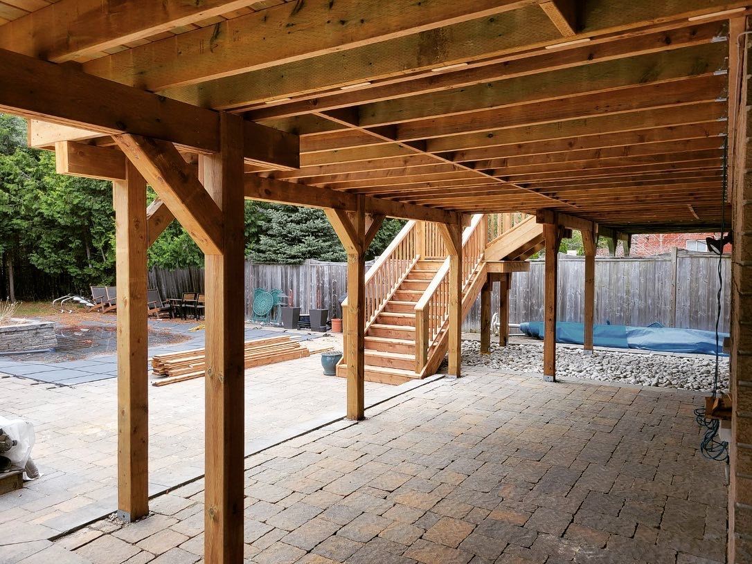 Wooden deck structure with stairs leading up, supported by posts, over a paved patio.