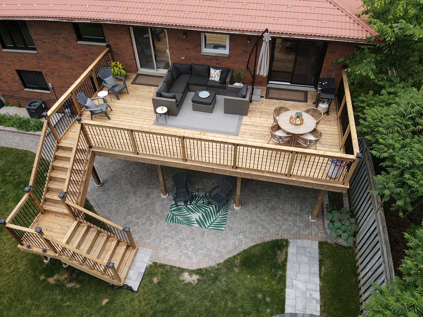 Elevated wooden deck with seating, stairs leading to a patio area and lawn. House in background.