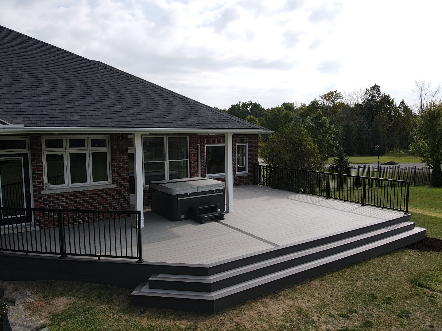 Composite deck with a hot tub next to a house with a dark roof. Black railing and steps lead to a grassy yard.