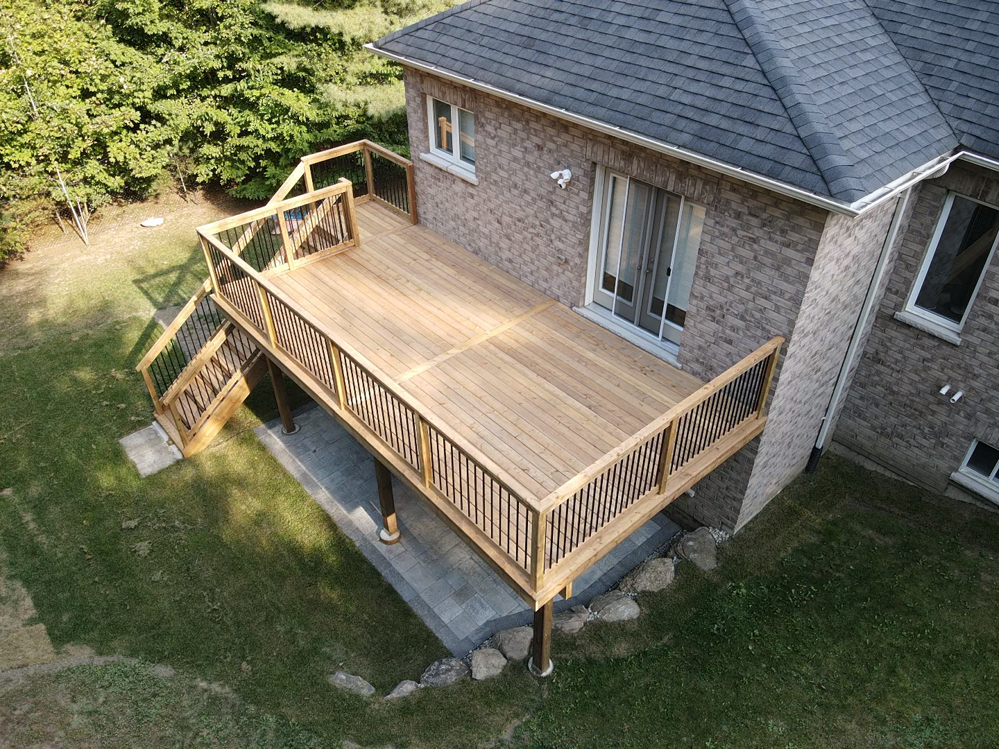 Wooden deck attached to a brick house, featuring stairs, railing, and a view of the yard.