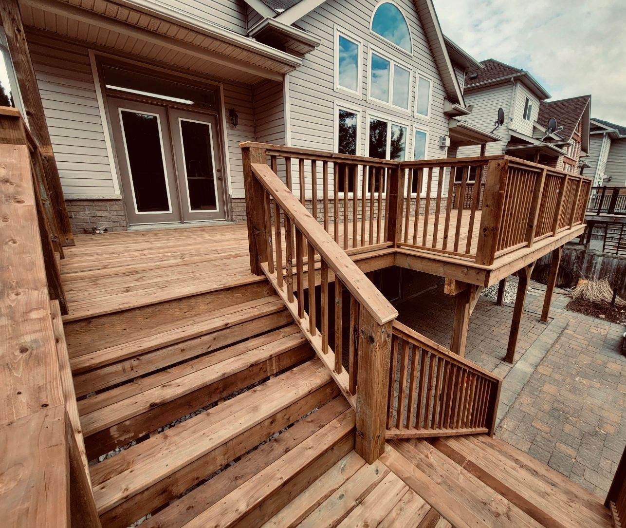 Wooden deck with stairs leading up to a multi-level deck attached to a light-colored house.