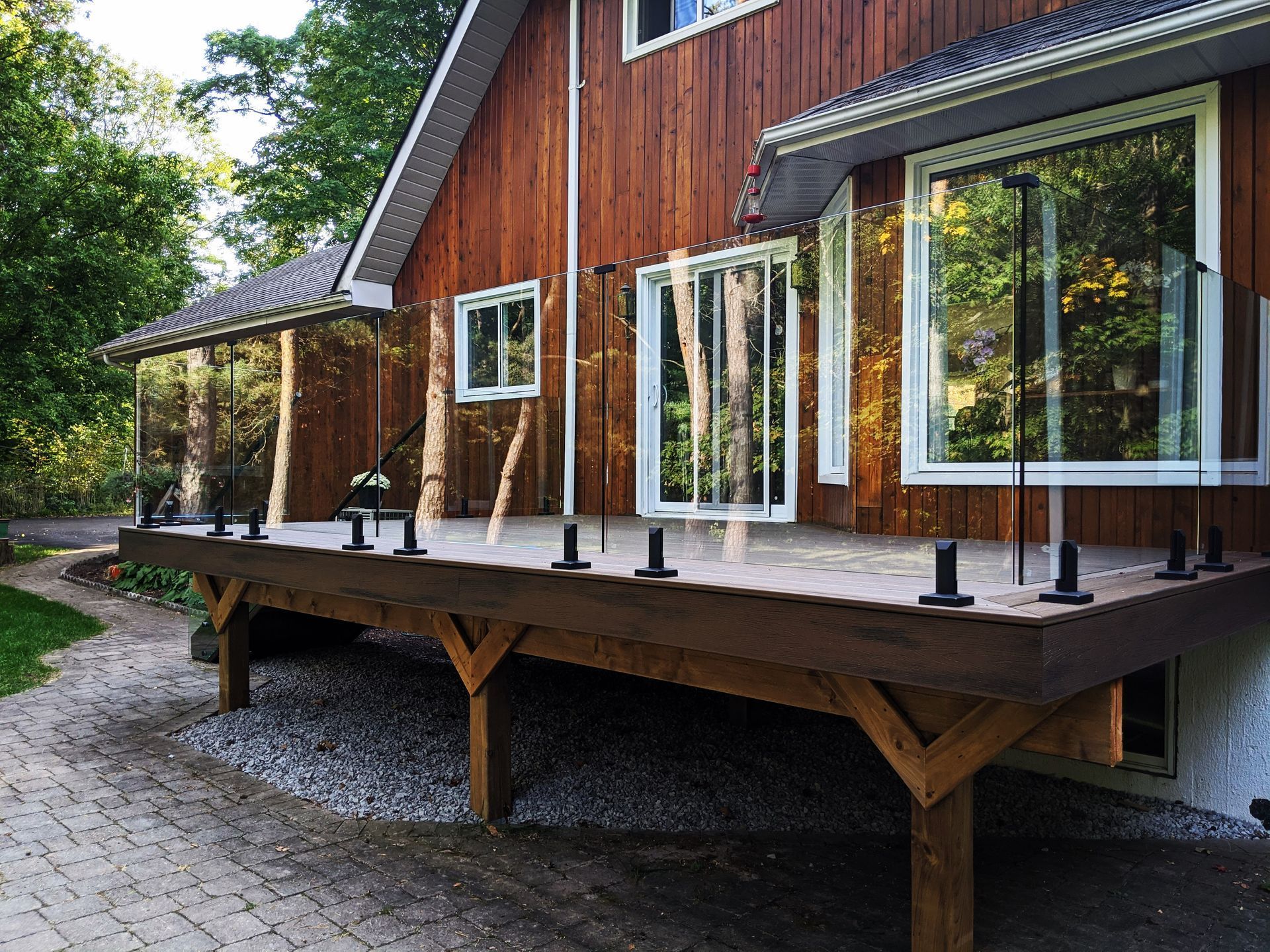 Wooden deck with glass railing attached to a brown house.