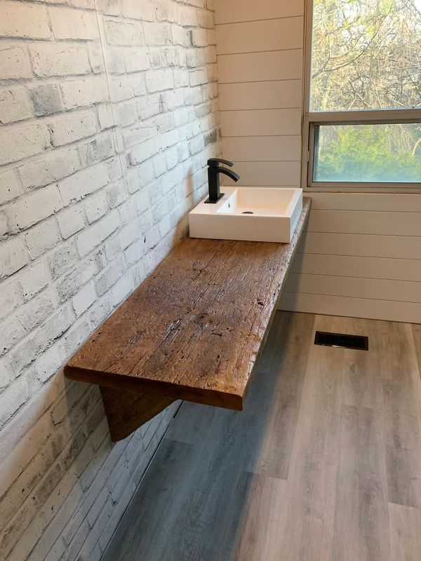 Bathroom with a floating wood countertop, white brick wall, rectangular sink, and window.