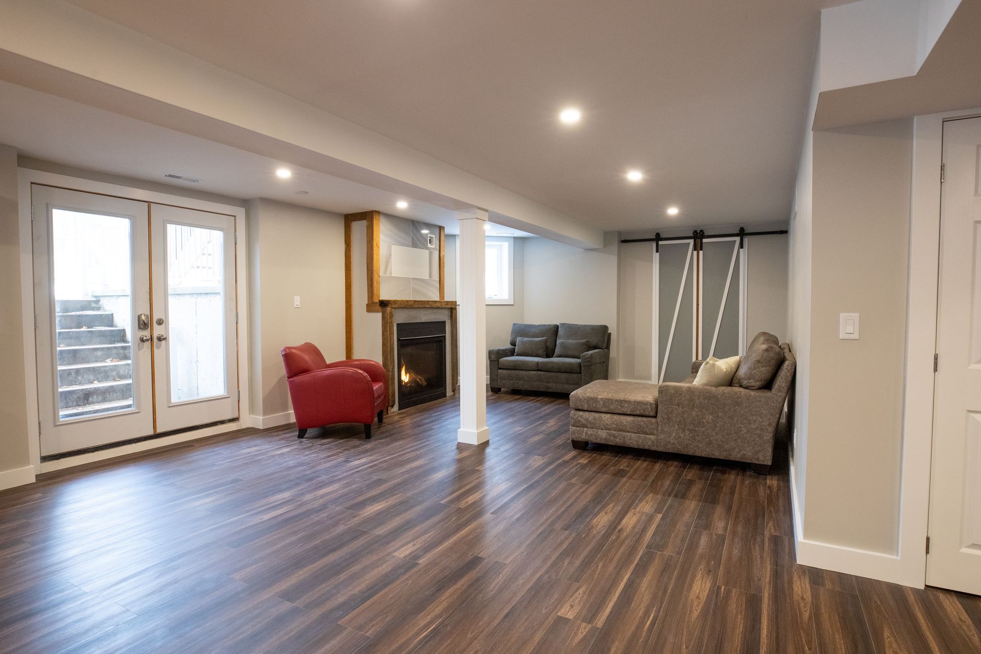 Spacious finished basement with hardwood floors, fireplace, seating area, and French doors leading outside.