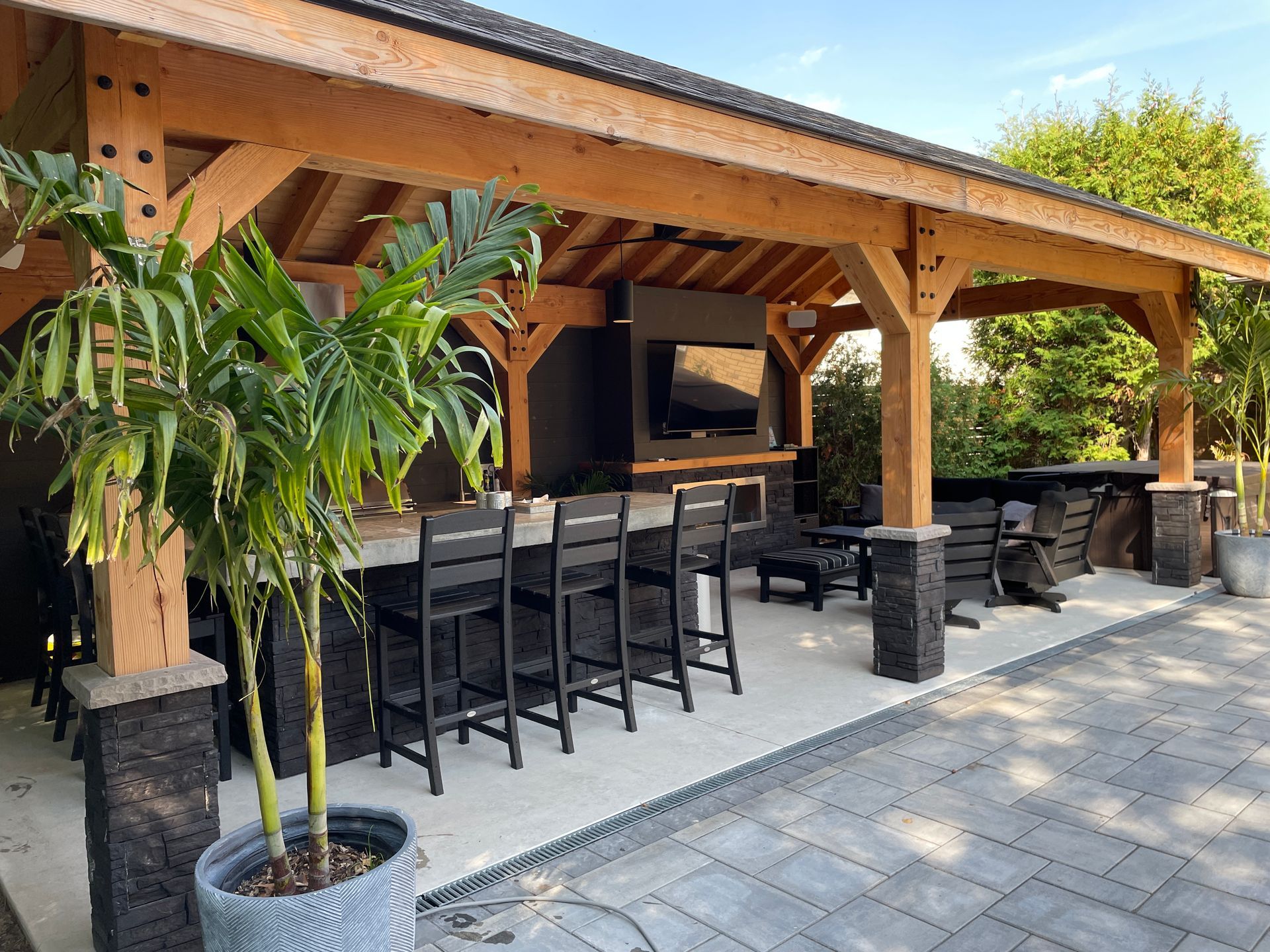 Outdoor bar with wooden structure, stone accents, bar stools, and a TV.