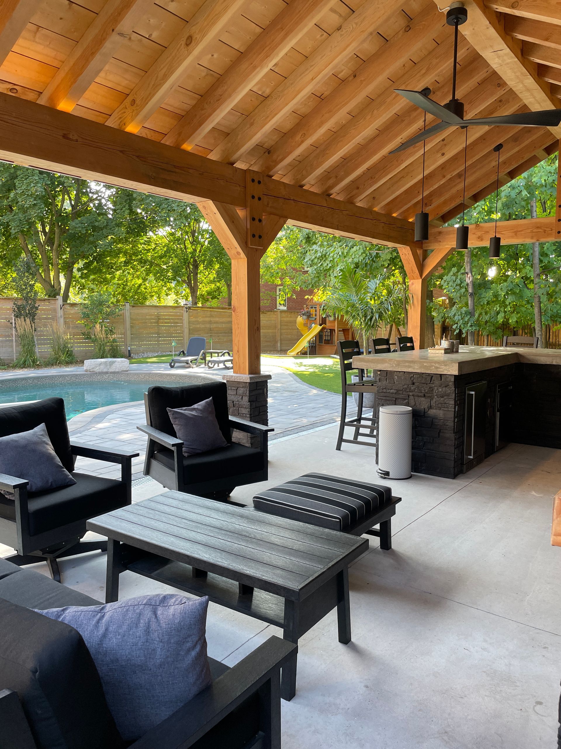 Outdoor patio with seating, bar, pool, and wooden pergola.