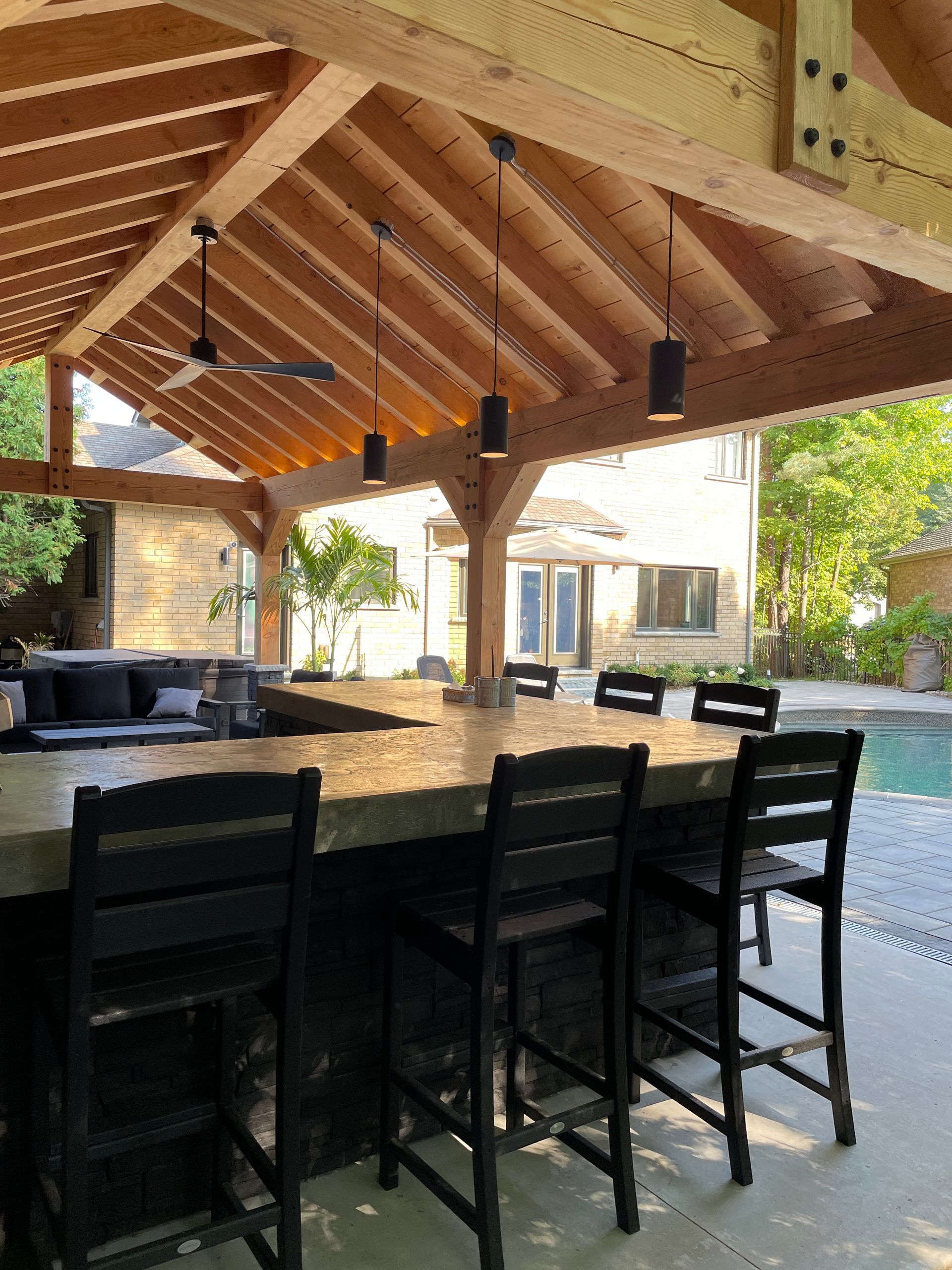 Outdoor bar with wooden roof, counter, bar stools, and pool in the background.