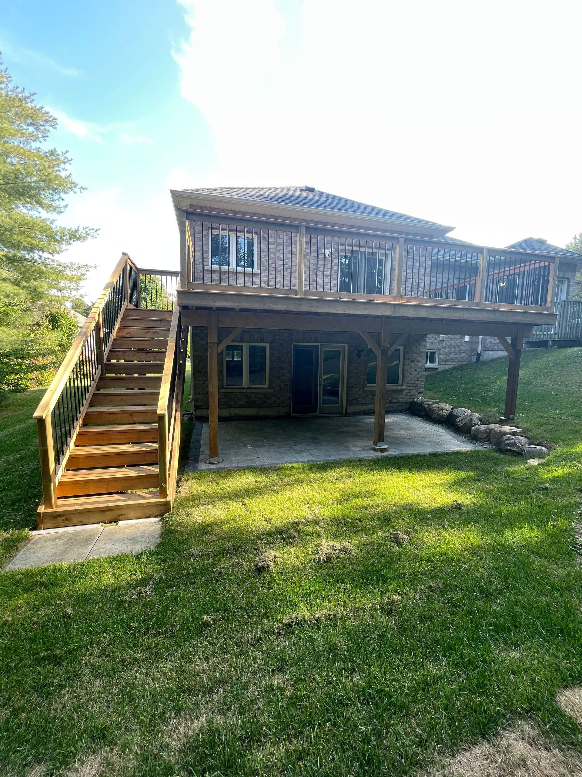 Two-story house with a wooden deck and stairs.  Green grass in foreground. Sunny day.