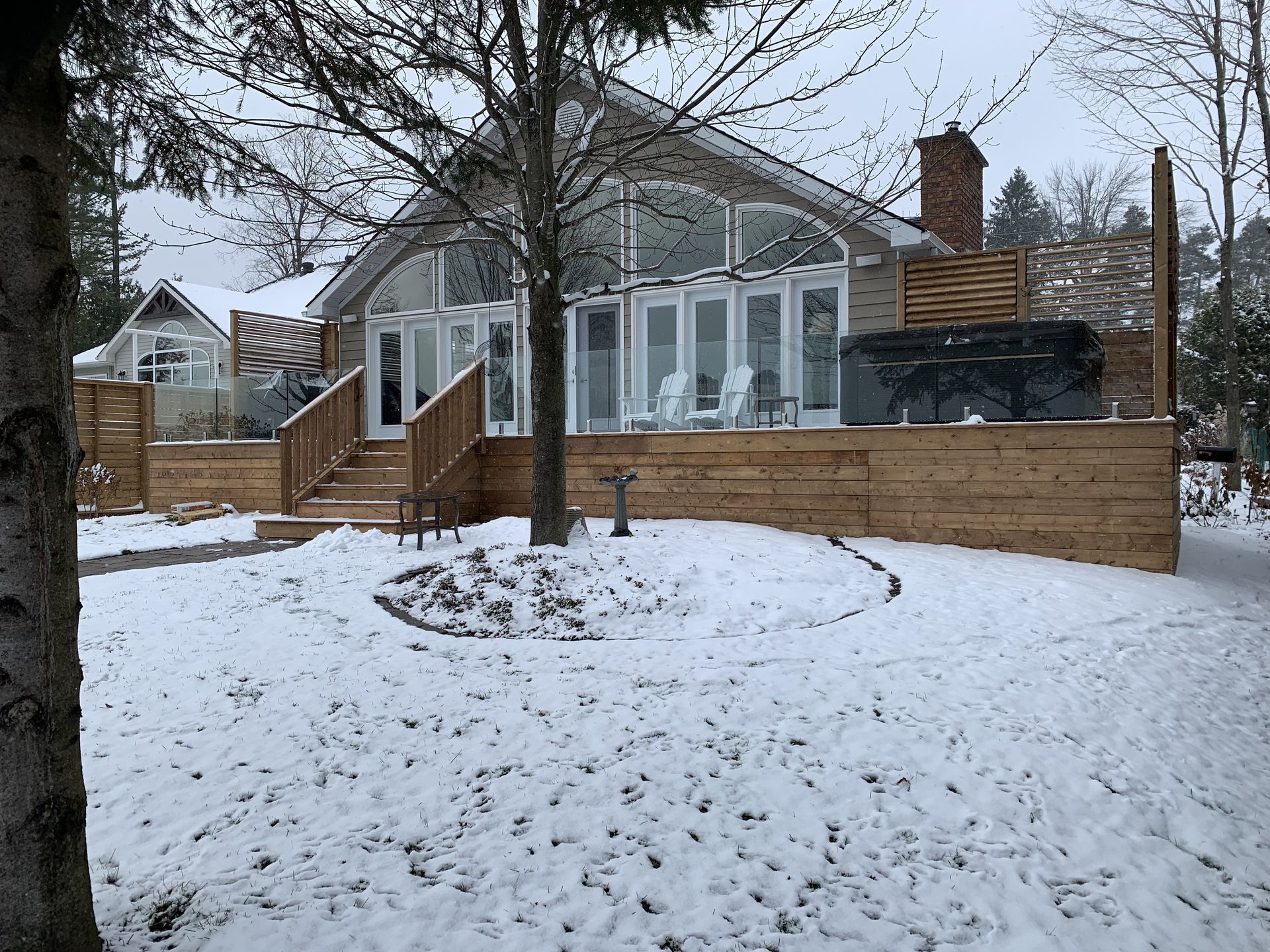 Snow-covered house with a large deck, hot tub, and glass doors. Winter scene.