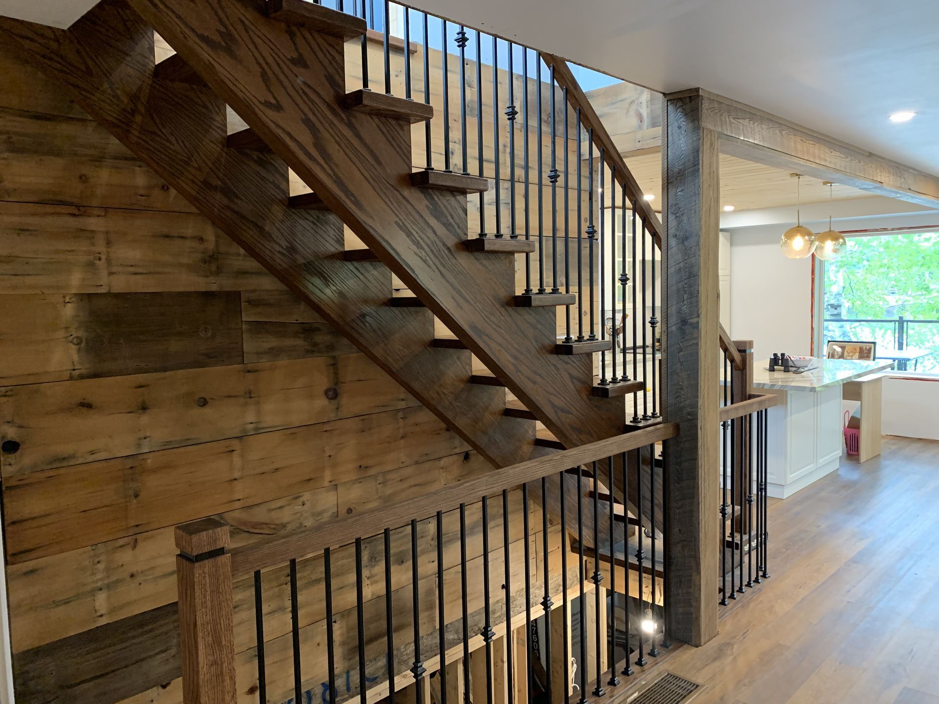 Wooden staircase with black metal spindles and wood panel wall.