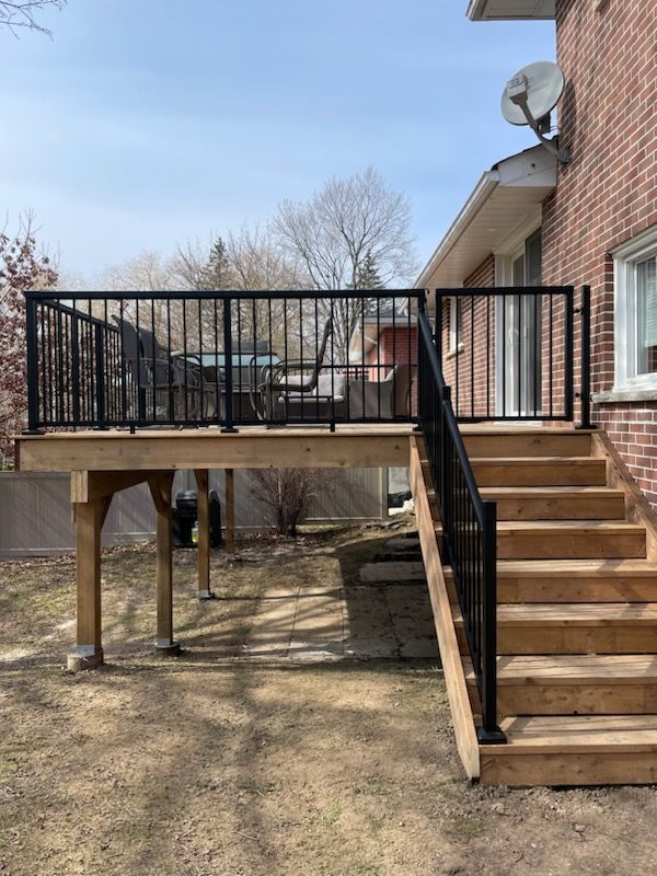 Wooden deck with black railing and stairs leading to a brick building.