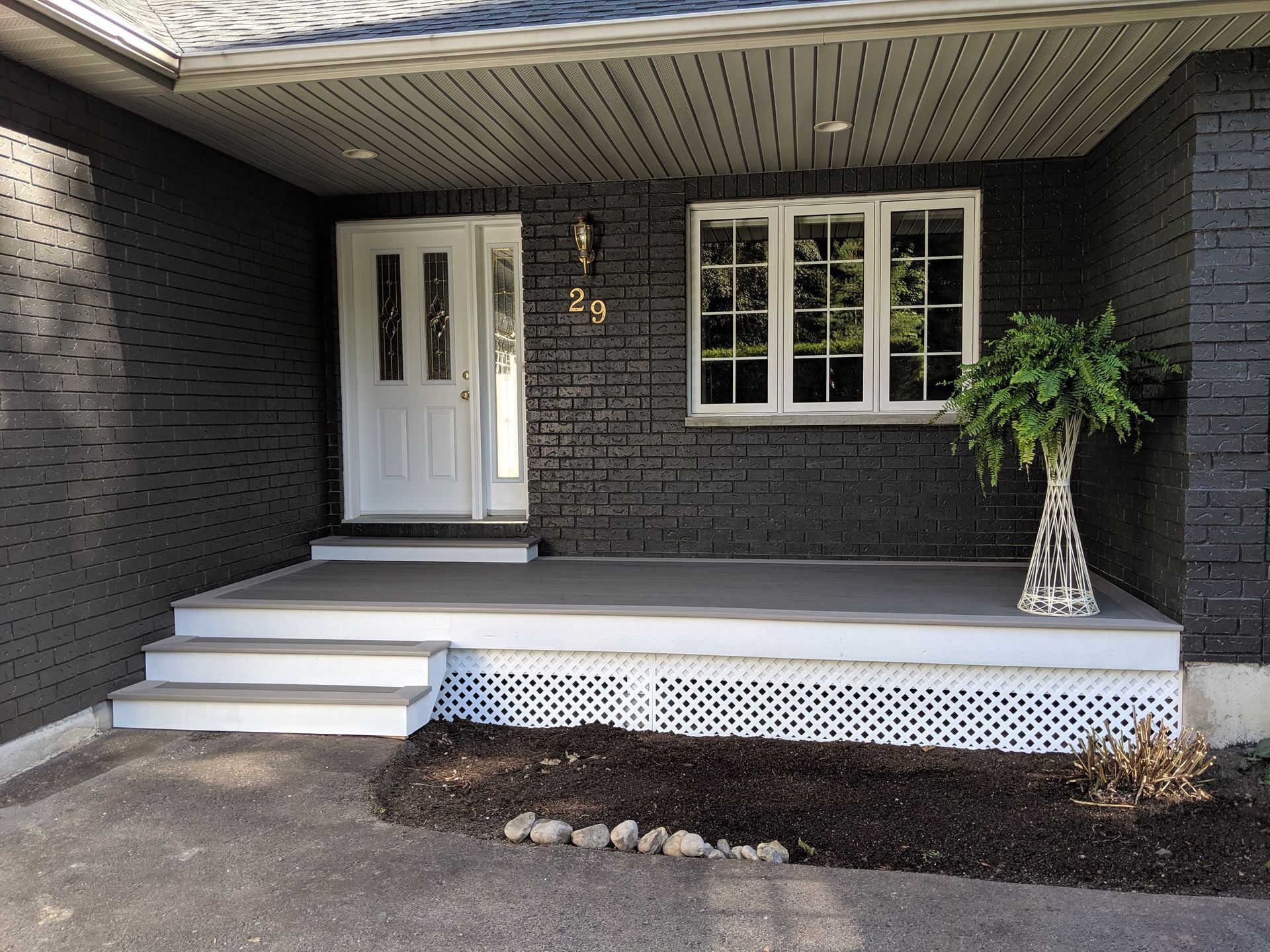 Dark gray brick home entrance with white door, steps, and latticework. Plant on right.