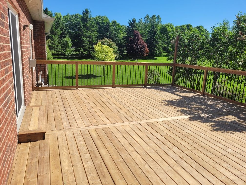 Wooden deck with black railing and green lawn, trees in background, bright sunny day.