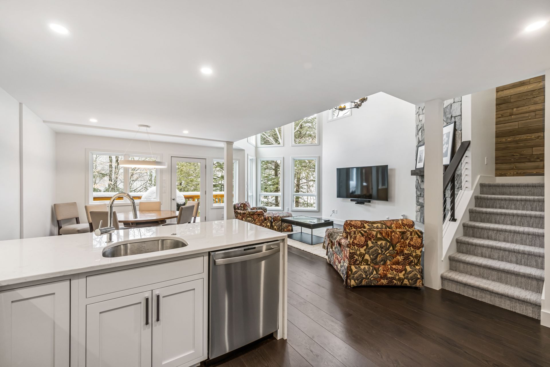 Open-plan living space with kitchen island, dark wood floors, and floral patterned armchairs.