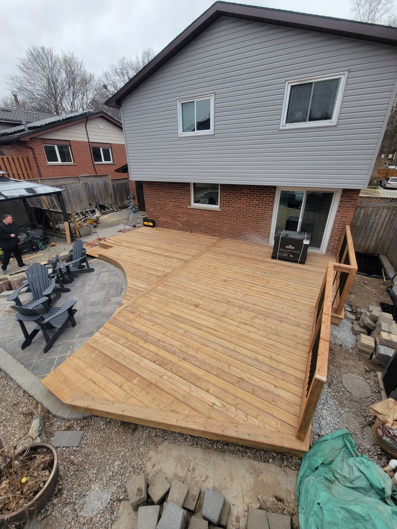 A wooden deck extending from a two-story house, with seating and a curved edge.