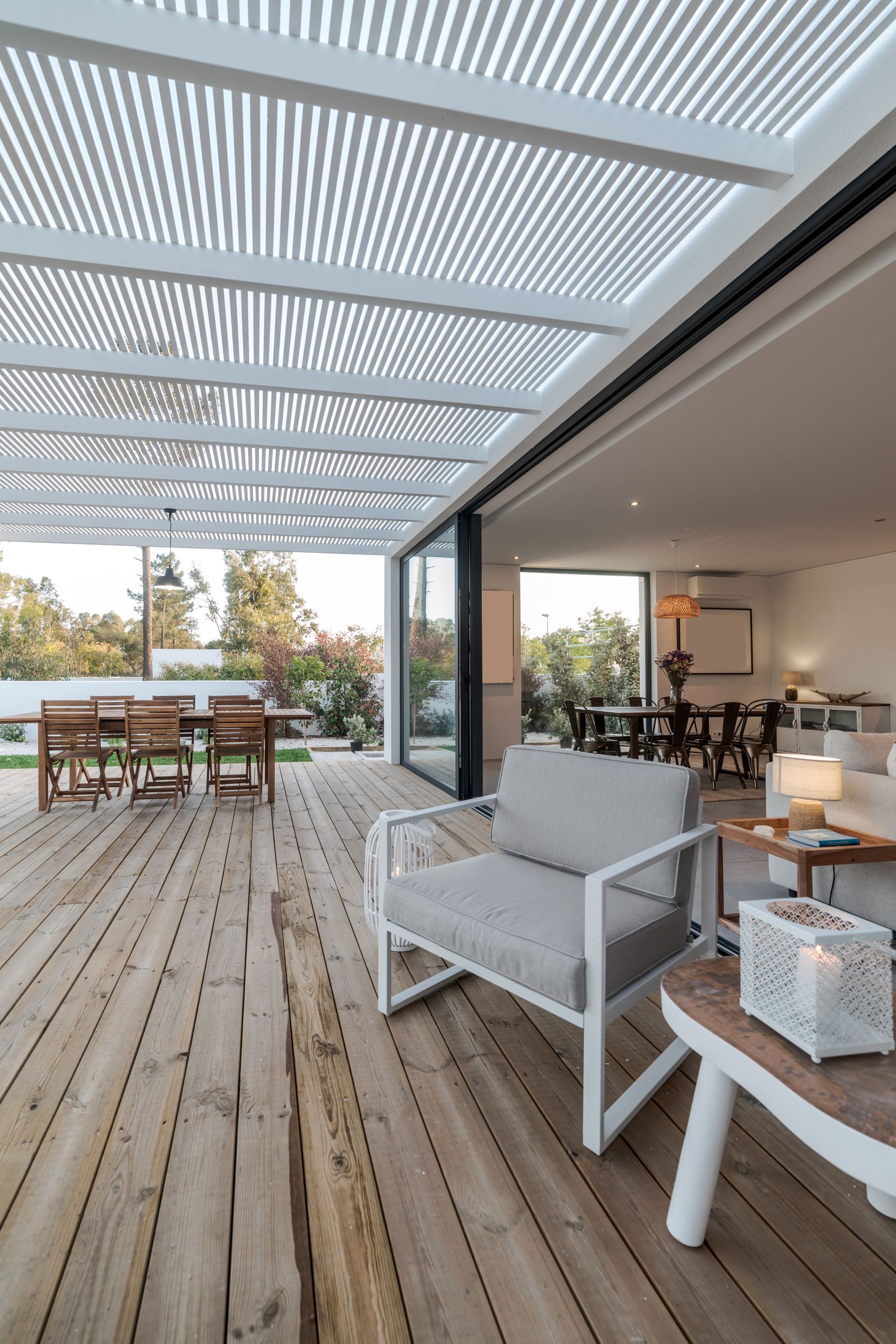 Outdoor patio with wooden deck, white pergola, and glass sliding doors leading to a living area.